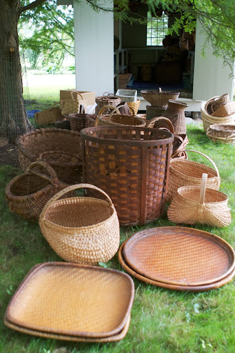 These flat tray baskets were used frequently in my catering days. Behind them are oak buttocks baskets, so named for their shape. They are also called melon baskets, egg baskets, and gathering baskets. The tall one was used to hold firewood.