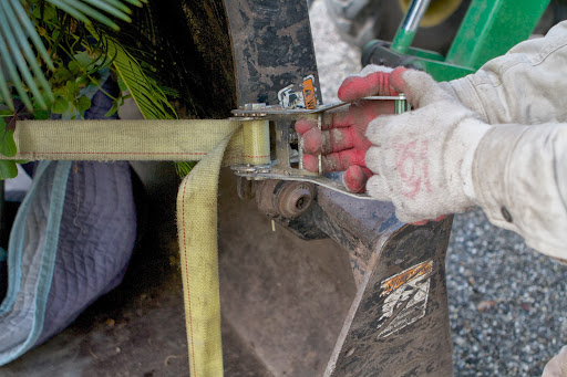 A moving blanket cushions the cement pot and an adjustable moving strap is tightened around it, securing the pot to the loader.