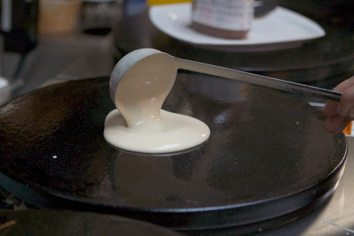 A ladle-full of batter is poured onto the hot crêpe maker.