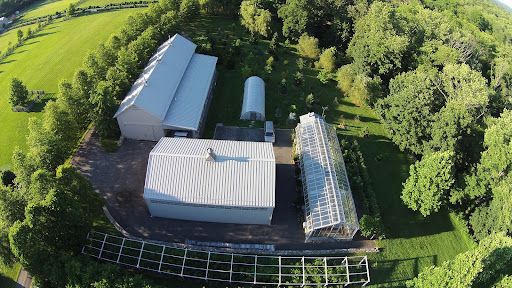 A closer look at the equipment shed, hoop house, vegetable greenhouse and hay barn. The curved structure in the foreground is the blueberry garden. It's actually not curved at all, but only appears so due to distortion created by the wide-angle lens on the drone camera.
