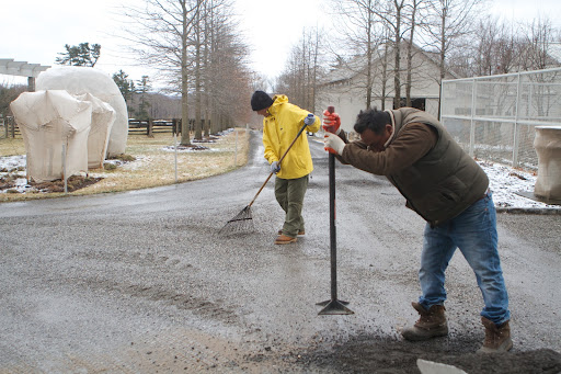 After raising the tamper above the ground, Pete forced the tamp back down to the ground, pressing the face of the tool with force against the gravel.
