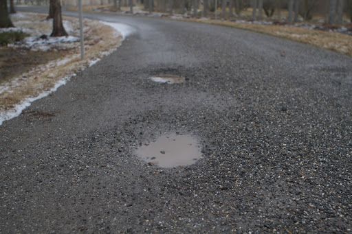 Potholes form easily on gravel roads when the ground is so wet. When over-sized stones are dislodged at or near the road surface, a small void occurs. The void fills with water and increases in size rapidly under the action of traffic.
