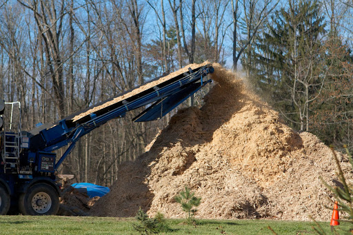 After passing through a grate, the shredded wood travels on a continuous conveyor, away from the grinding chamber.