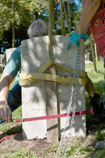 When a headstone is broken in two, Will and Lisa cinch it with wood and straps and lift it in place using a tripod and chain hoist.