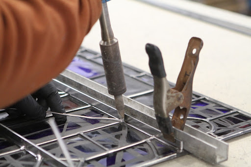 This craftsman is attaching reinforcement bars, or rebars, which are highly recommended on all leaded glass windows that are used in a moving unit, such as doors and windows. Without a rebar, over time the window can bow outward, breaking the glass.